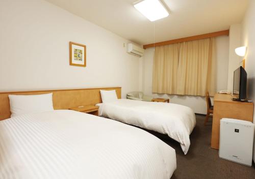 a hotel room with two beds and a television at Business Hotel Isesaki Heisei Inn in Isesaki
