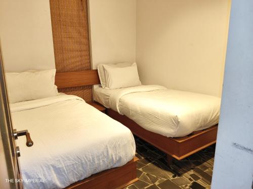 two beds in a small room with white sheets at The Sky Imperial Aarivaa Luxury Stays in Rajkot