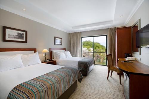 Habitación de hotel con 2 camas, escritorio y TV. en Garden Route Hotel en Mossel Bay