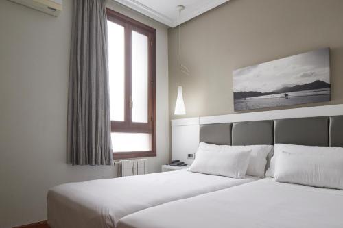 two beds in a hotel room with a window at Pensión Alemana in Donostia-San Sebastián