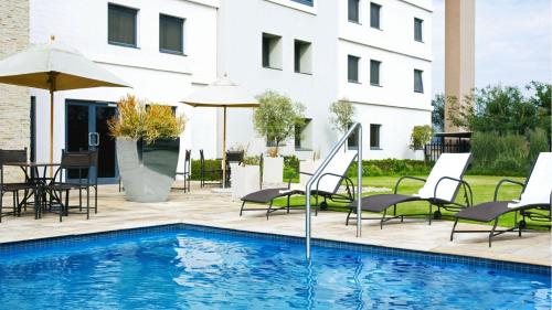 a pool with chairs and umbrellas next to a building at The RidgePoint Hotel in Witbank