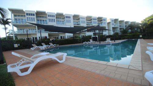 un complexe avec une piscine, des chaises et un bâtiment dans l'établissement Unit 12 Beachside Apartments, à Nelly Bay