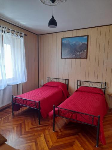two beds in a room with wooden floors and a window at La Mëisun in Perrero