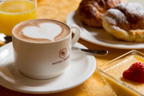 a cup of coffee sitting on a table with plates of pastries at Hotel Berna in Milan