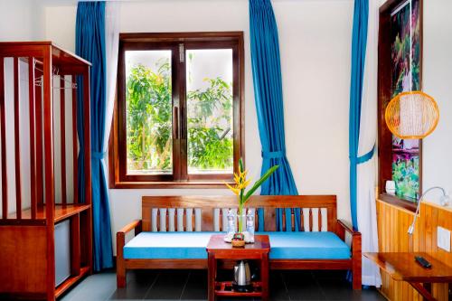 um quarto com um banco e uma janela com cortinas azuis em Villa Loan A HOI AN em Hoi An
