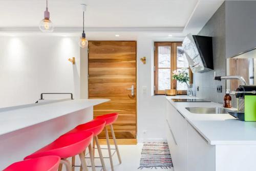 une cuisine avec des comptoirs blancs et des tabourets de bar rouges dans l'établissement Maison Castellino, à Annecy