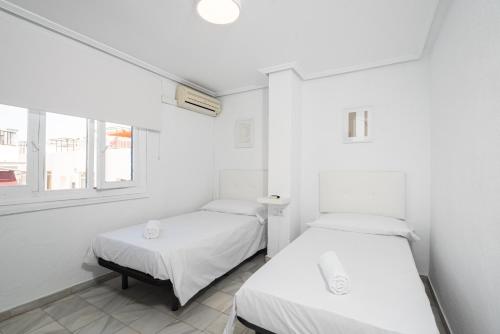 two beds in a room with white walls and a window at Hostal Alicia in Marbella