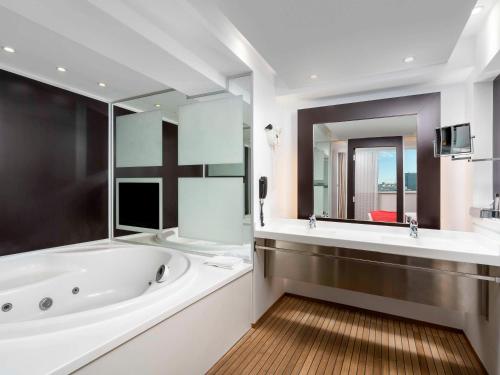 a bathroom with a tub and a large mirror at Novotel Bucharest City Centre in Bucharest