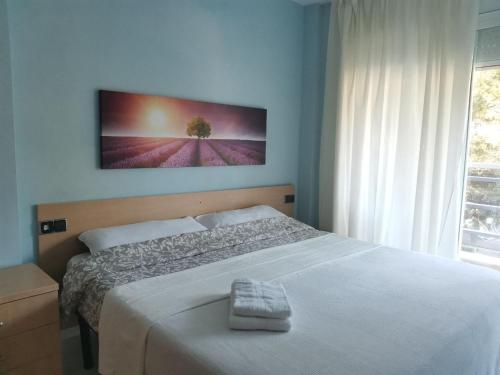 a bedroom with a white bed with a picture on the wall at S'Abanell Central Park seafront apartment in Blanes