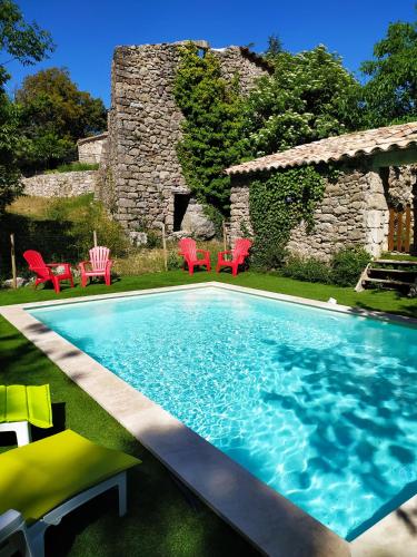 une piscine avec des chaises rouges et une maison en pierre dans l'établissement Les MIMOSAS Gîte du Mas Haut, à Saint-Jean-du-Gard