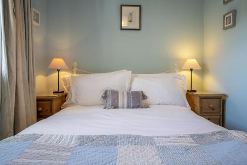 a bed with white pillows and two lamps on tables at Burn Cottage in Leyburn
