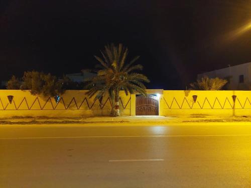 a yellow fence with a door on a street at night at chambre Noix de Coco résidence Chahrazad in Sfax