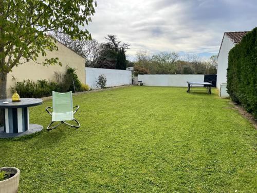 a lawn with a table and a chair in a yard at Maison confort & jardin à Saint-Pierre-d'Oléron in Saint-Pierre-dʼOléron