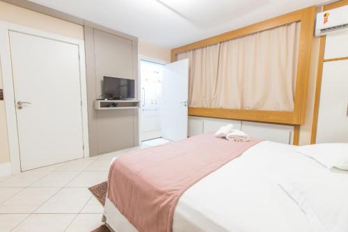 a bedroom with a white bed and a television at Delupo Hotel - Livin Studios in Criciúma