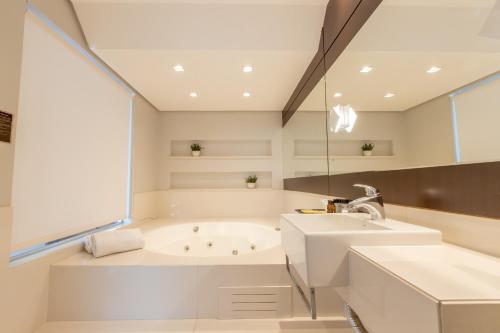 a white bathroom with a tub and a sink at Delupo Hotel - Livin Studios in Criciúma