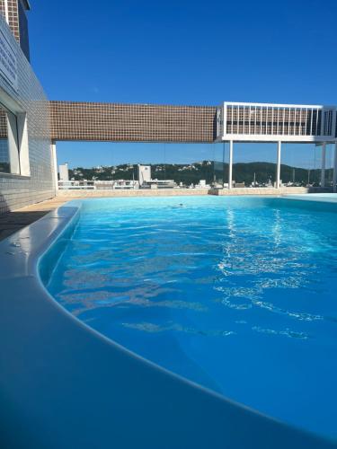 a swimming pool with blue water in front of a building at Apto com Piscina, Estacionamento e Churrasqueira em Bombas - 2 dorms 6 pessoas - 300 metros do Mar in Bombinhas