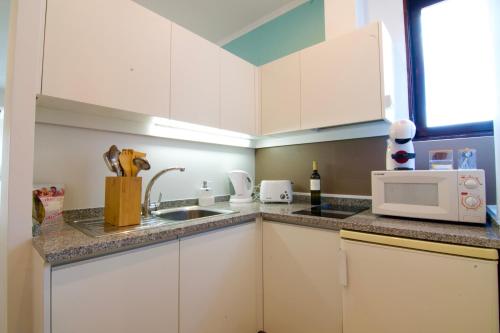 a kitchen with white cabinets and a sink and a microwave at Sunset Retreat 1a linha de mar in Monte Gordo