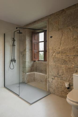 a glass shower in a bathroom with a stone wall at Pazo da Buzaca in Moraña