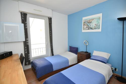 twee bedden in een kamer met blauwe muren en een raam bij Les 2 Caps Saint Philippe in Biot