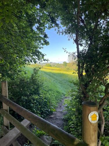 a wooden fence next to a field with a path at BARLEY - cosy stylish apartment - easy access to Bath and many nearby attractions in Box