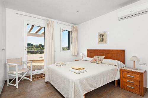 a bedroom with a bed and a chair and a window at Villa Sa Gavina - Addaia in Port d'Addaia