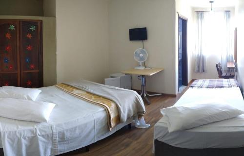 a bedroom with two beds and a desk with a fan at Hotel Pousada Icaraí in Poços de Caldas