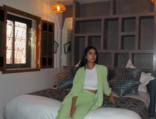 RIAD LUXE LOCATION le GRIZZLY في مراكش: امرأة جالسة على سرير ترتدي سترة خضراء