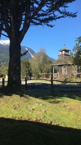 un gran árbol en un campo con una iglesia en Bosque Patagonico Cabañas y Camping, en Hornopirén