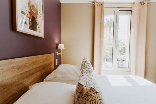 a bedroom with a bed with white sheets and a window at Hôtel Le Petit Castel in Antibes