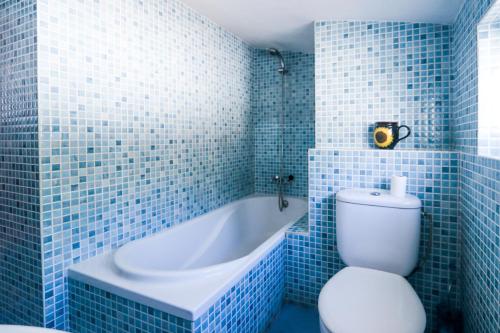 y baño de azulejos azules con aseo y bañera. en Casa Elizabeth, en Jávea