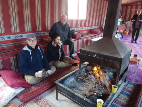 three people sitting on a couch next to a fireplace at Sun rise wadi rum camp in Wadi Rum