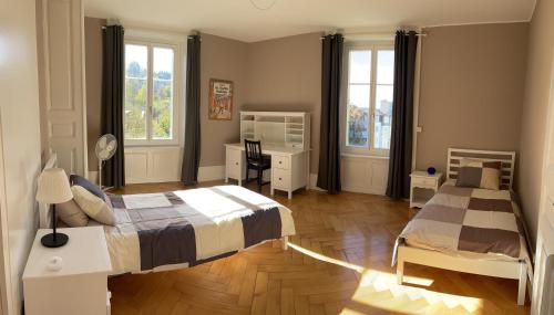sypialnia z 2 łóżkami i biurkiem oraz 2 oknami w obiekcie Le Locle : bel appartement chaleureux w mieście Le Locle