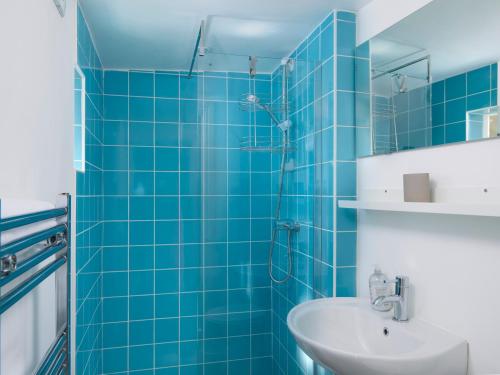 La salle de bains est pourvue de carrelage bleu, d'un lavabo et d'une douche. dans l'établissement Saltwater Cottage, à Torquay