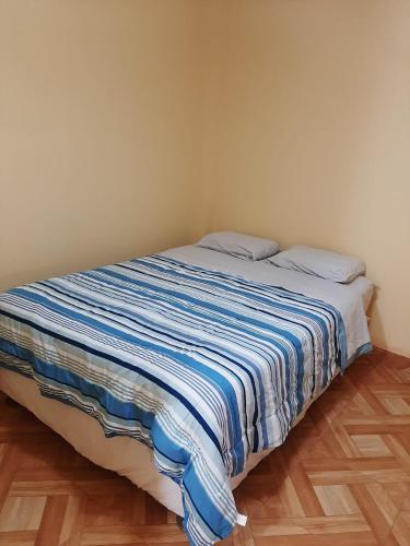 a bed with a blue and white striped blanket on it at Casa La Ruta Jardines in Pisco