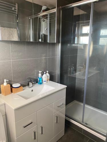 La salle de bains est pourvue d'un lavabo blanc et d'une douche. dans l'établissement Short and Long Night Stay - very close to Gatwick and City Centre - Private Airport Holiday Parking - Early Late Check-ins, à Crawley