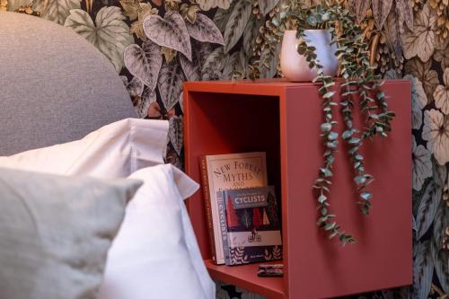 a red bedside table with books and a vase on it at The Nest in Brockenhurst