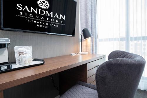 a room with a desk with two chairs and a tv at Sandman Signature Sherwood Park Hotel in Sherwood Park
