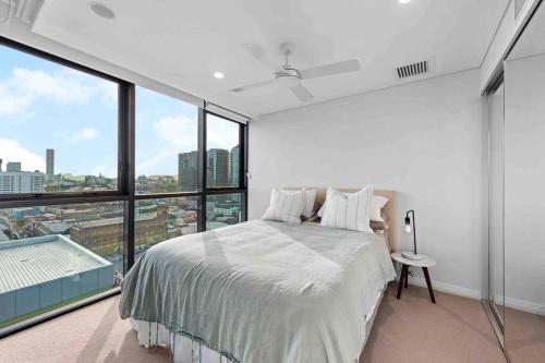 a white bedroom with a bed and large windows at Prime position 1.5 BR w/ view/ parking / roof pool in Brisbane