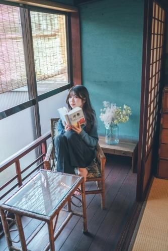a woman sitting in a chair reading a book at Machiya Guest House Carta in Kanazawa