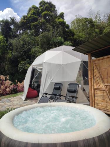 a hot tub in a yard with chairs and a tent at Colibamboo Domo Glamping in Pacho