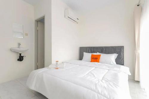 a white bedroom with a large white bed with an orange pillow at KoolKost Syariah near Bintaro Jaya Xchange in Peladen