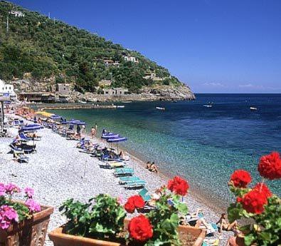 a beach with chaise lounges and chairs and the ocean at Marina del Cantone Chalet in Nerano