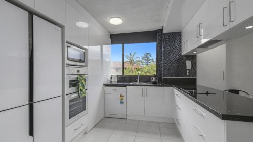 een keuken met witte kasten, een wastafel en een raam bij Beachpark Apartments - Close To Beach in Port Macquarie