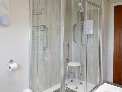 y baño con ducha de cristal con taburete. en Mill Shore Cottage - 26817, en Pennan