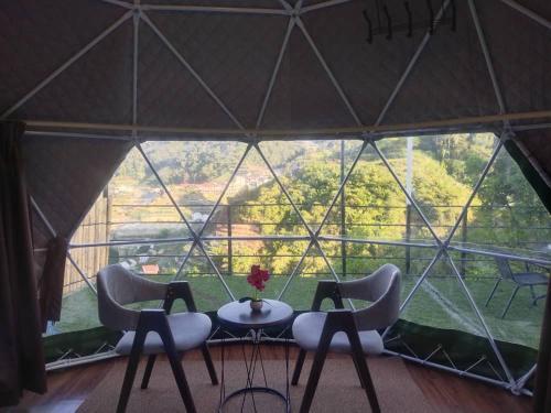 a tent with three chairs and a table in front of a large window at Glamz Hills in Cameron Highlands