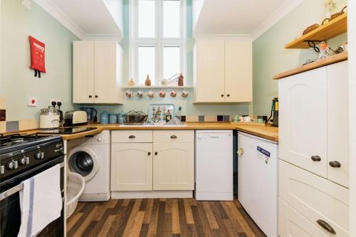 cocina con armarios blancos, lavadora y secadora en Chapel Cottage en Canterbury