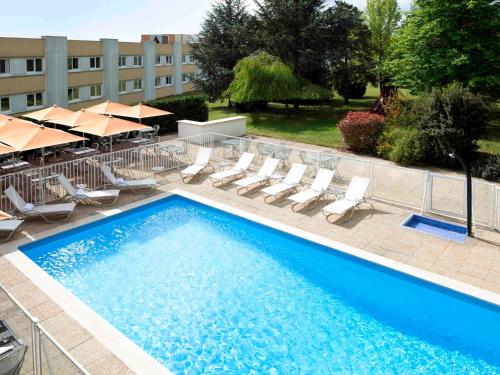 une grande piscine avec des chaises et des parasols dans l'établissement Novotel Macon Nord Autoroute du Soleil, à Mâcon