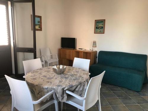 Appartamenti L'Approdo del Gabbiano في لامبيدوسا: طاولة طعام مع كراسي بيضاء وأريكة خضراء