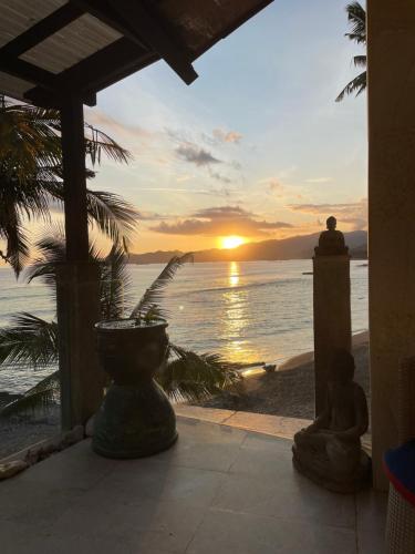 une personne assise sur une terrasse couverte pour admirer le coucher du soleil dans l'établissement Ocean Suite - Exceptional Beachfront Apartment - Candidasa, à Candidasa