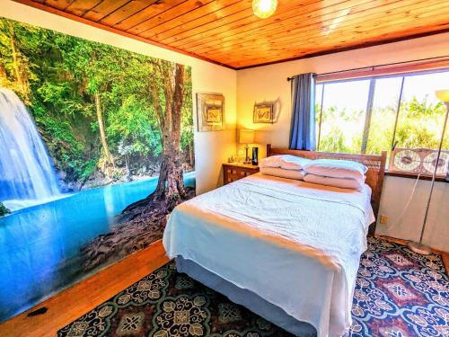 a bedroom with a bed and a window with a waterfall at Hamakua Guesthouse in Pepeekeo